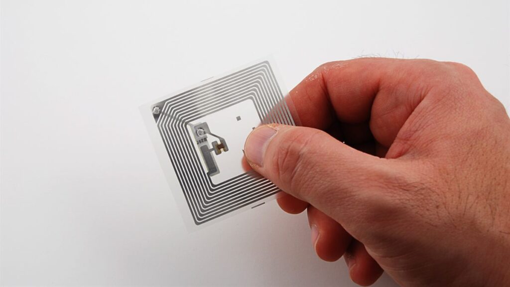 A passive RFID inlay. The chip sits at the center of a spiral antenna that both harvests power from the reader’s signal and sends the reply, which is why the whole tag can be as thin as a paper label.